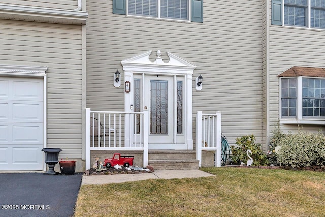 view of exterior entry with an attached garage and a yard