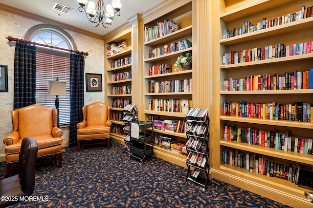 living area with a chandelier, carpet floors, visible vents, ornamental molding, and wall of books