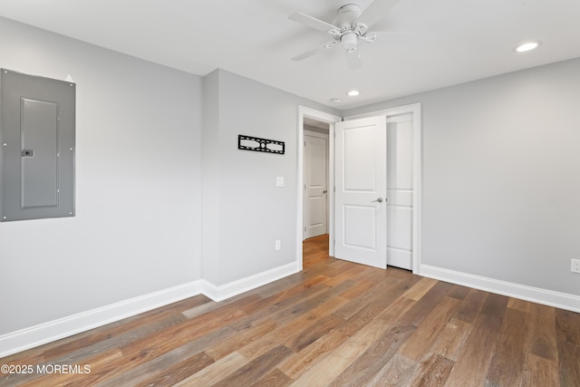 empty room featuring recessed lighting, wood finished floors, electric panel, and baseboards