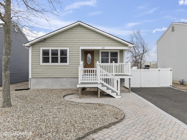 view of front of house featuring aphalt driveway, a porch, and fence