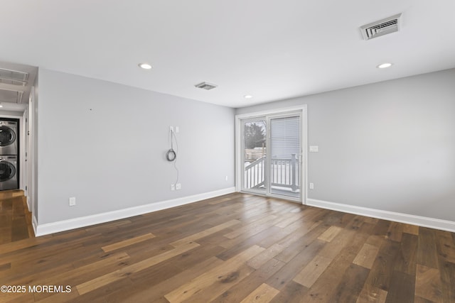 empty room featuring stacked washing maching and dryer, baseboards, visible vents, and dark wood-type flooring