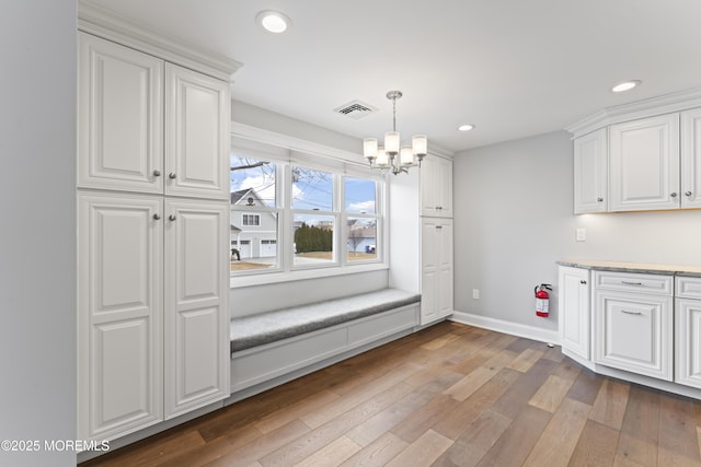 unfurnished dining area with a notable chandelier, recessed lighting, visible vents, hardwood / wood-style floors, and baseboards