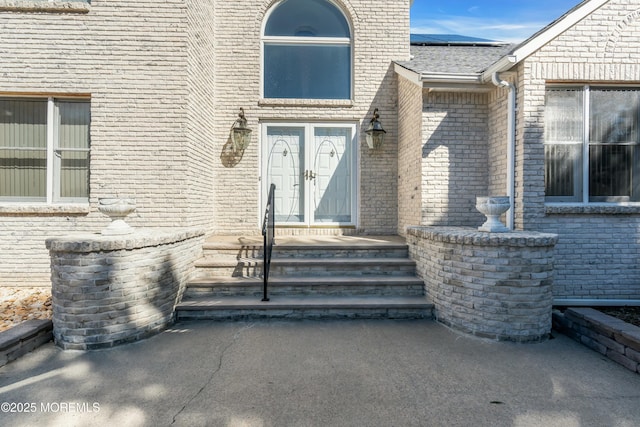 property entrance featuring brick siding, roof mounted solar panels, and french doors