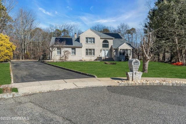 view of front of property with roof with shingles, driveway, a chimney, a front lawn, and brick siding