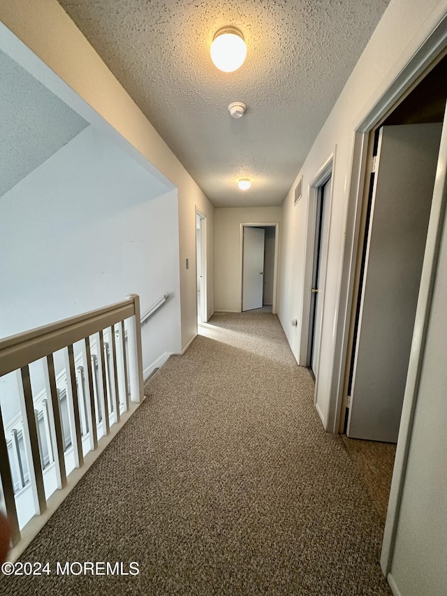 hall with a textured ceiling, carpet flooring, and visible vents