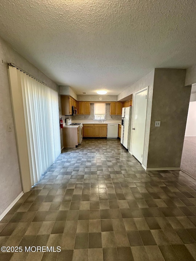 kitchen with brown cabinets, light countertops, a sink, white appliances, and baseboards