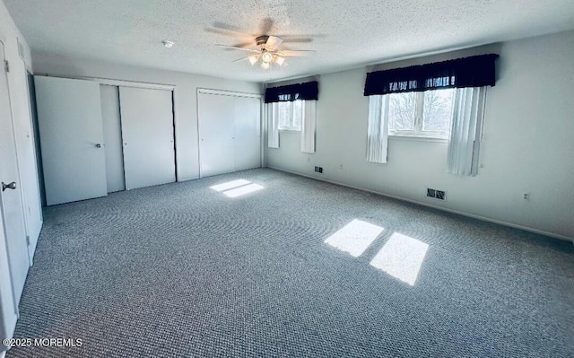 unfurnished bedroom featuring a textured ceiling, carpet, visible vents, and multiple closets