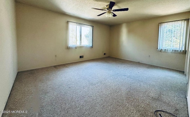 unfurnished room with a textured ceiling, carpet floors, visible vents, and a ceiling fan