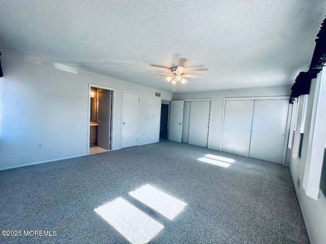 unfurnished bedroom featuring a ceiling fan, ensuite bathroom, a textured ceiling, carpet floors, and two closets