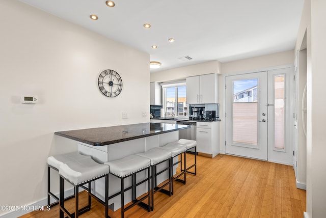 kitchen with light wood finished floors, visible vents, dishwasher, a breakfast bar area, and a peninsula