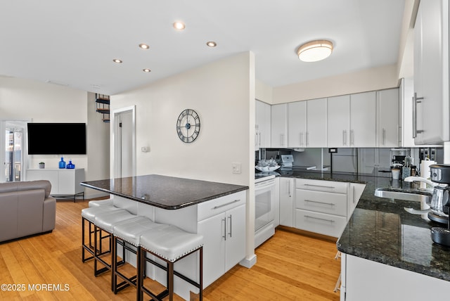 kitchen with a peninsula, white appliances, light wood-style floors, and a sink