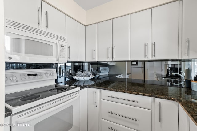 kitchen featuring white appliances, white cabinets, and dark stone countertops