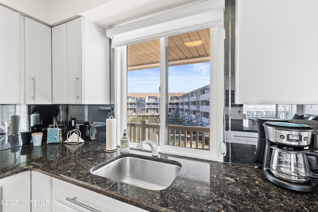 kitchen featuring dark stone counters, white cabinetry, and a sink