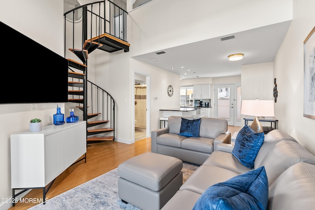 living room featuring light wood-style flooring, stairway, visible vents, and baseboards