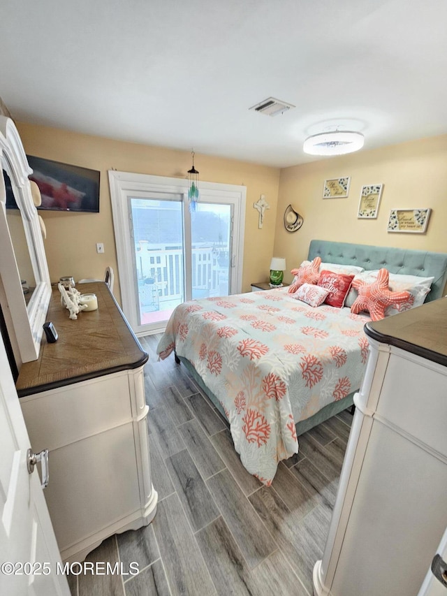 bedroom with wood finish floors, visible vents, and access to exterior