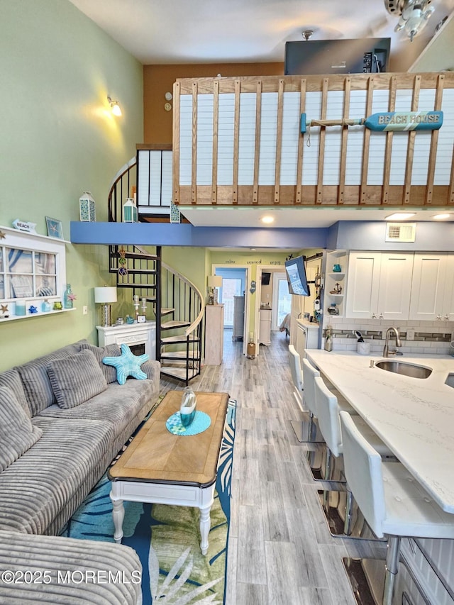 living area featuring a towering ceiling, visible vents, light wood-style flooring, and stairs