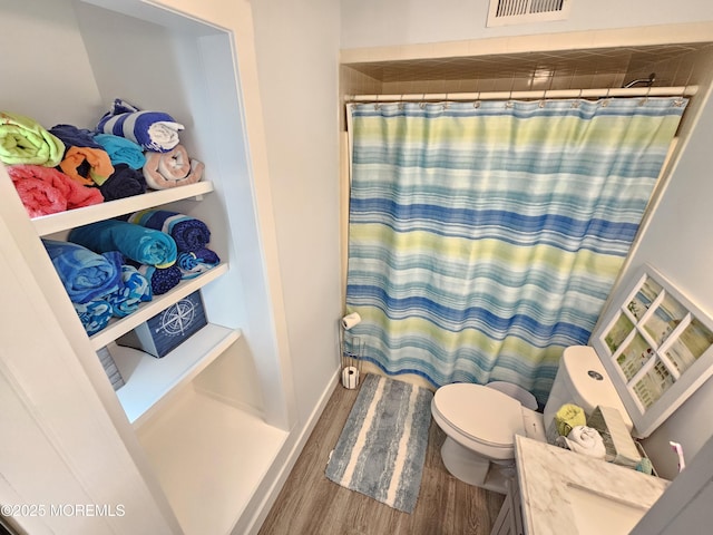 bathroom featuring a shower with shower curtain, toilet, wood finished floors, and visible vents