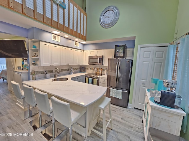 kitchen featuring light wood-type flooring, light stone counters, tasteful backsplash, stainless steel appliances, and a peninsula