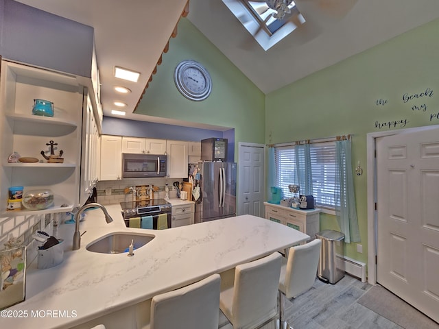 kitchen with light stone counters, light wood-style flooring, a sink, decorative backsplash, and appliances with stainless steel finishes