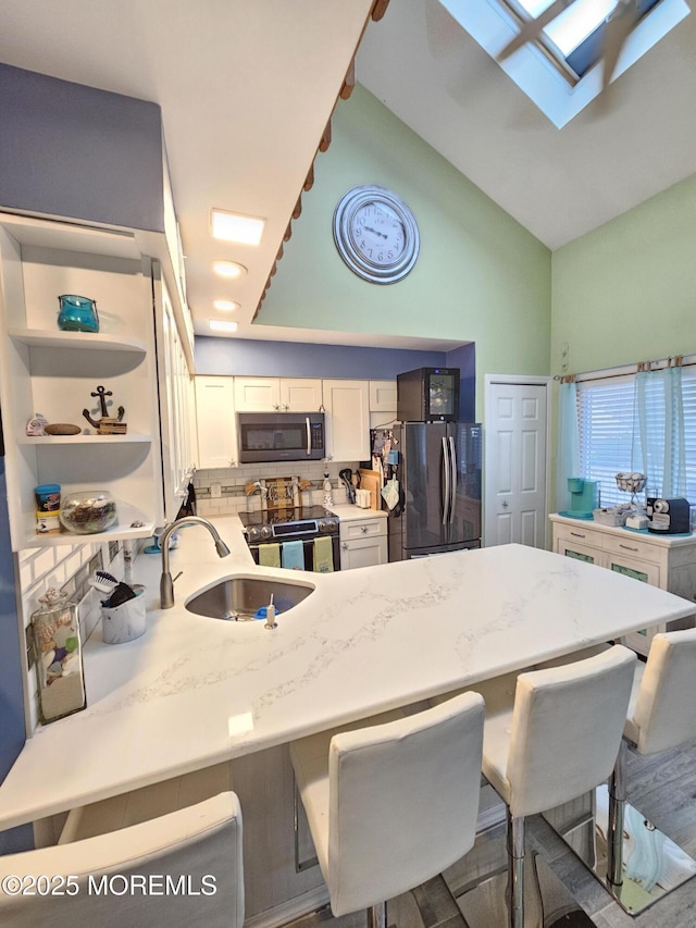 kitchen featuring a breakfast bar, a sink, white cabinetry, freestanding refrigerator, and stainless steel electric range oven