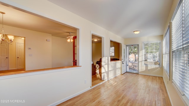 empty room featuring ceiling fan with notable chandelier, baseboards, and light wood-type flooring