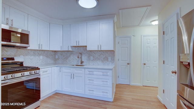 kitchen with light wood-style flooring, a sink, stainless steel appliances, light countertops, and white cabinets