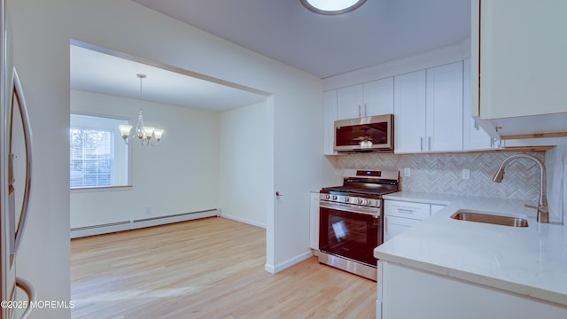 kitchen with a sink, backsplash, stainless steel appliances, white cabinets, and baseboard heating