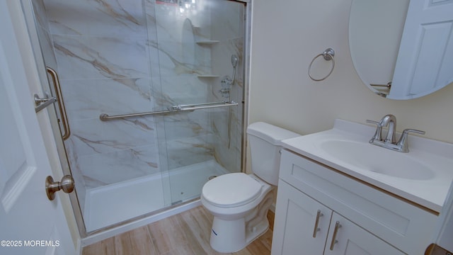 bathroom with vanity, toilet, wood finished floors, and a marble finish shower