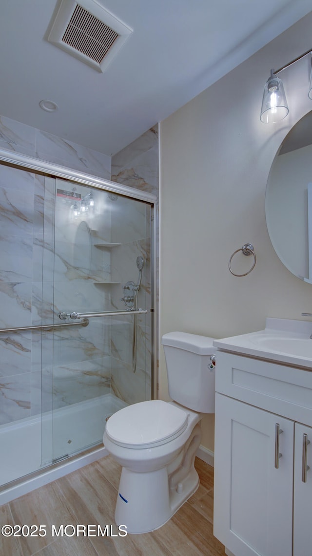 bathroom with visible vents, toilet, a stall shower, wood finished floors, and vanity