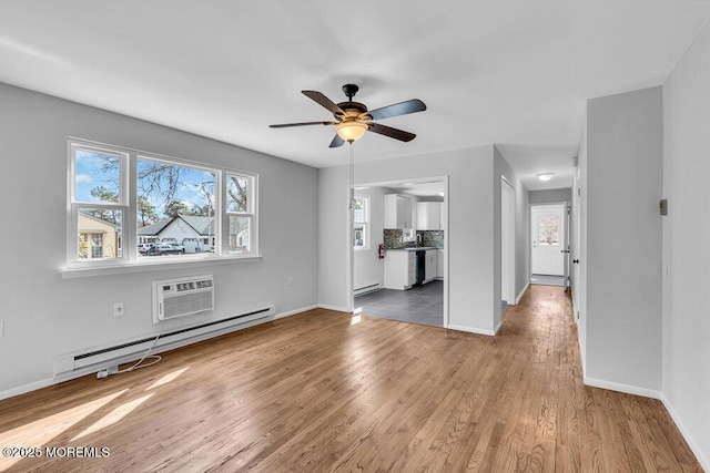 unfurnished living room with a wall unit AC, a baseboard radiator, wood finished floors, and baseboards