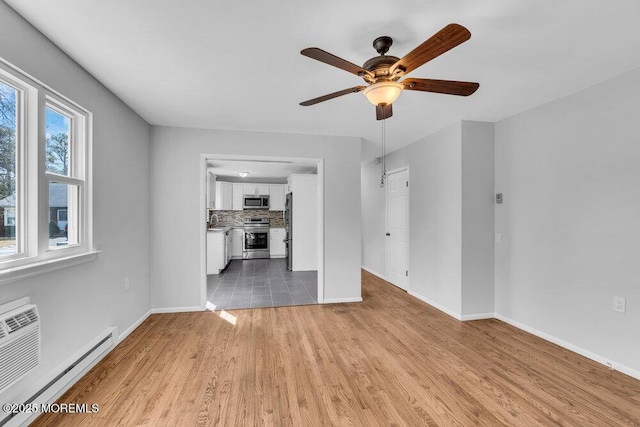 unfurnished living room featuring a baseboard heating unit, ceiling fan, light wood finished floors, and baseboards