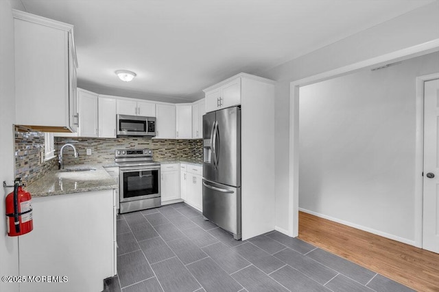 kitchen featuring white cabinets, a sink, light stone countertops, stainless steel appliances, and backsplash