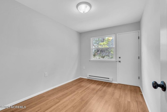 spare room with a baseboard heating unit, light wood finished floors, and baseboards