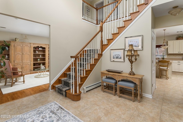 stairway featuring a baseboard heating unit, baseboards, a high ceiling, and tile patterned floors