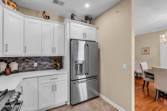 kitchen with visible vents, backsplash, stove, white cabinetry, and high end refrigerator