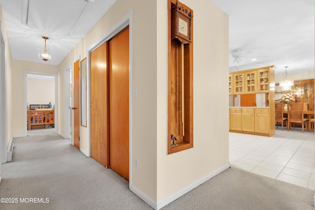 hallway with light carpet, light tile patterned floors, baseboards, baseboard heating, and a notable chandelier