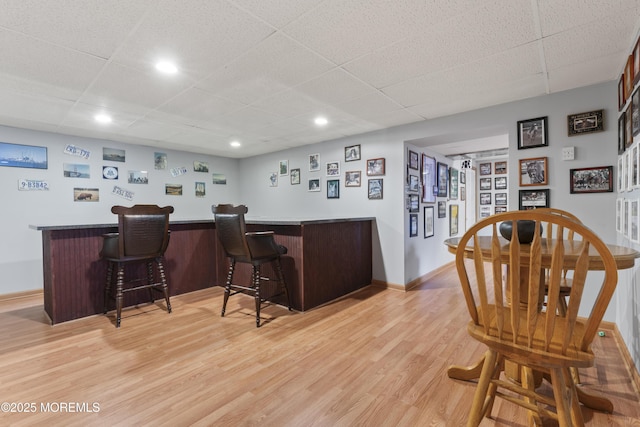 bar with baseboards, a dry bar, a drop ceiling, and light wood-style floors