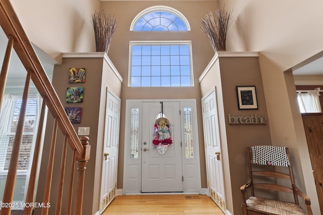 foyer entrance with a towering ceiling, light wood-style floors, stairs, and visible vents