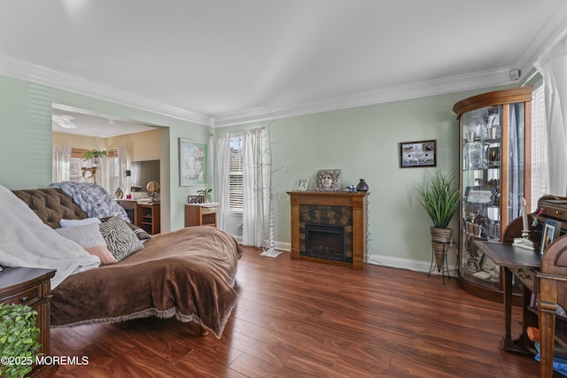 bedroom with baseboards, a stone fireplace, wood finished floors, and crown molding