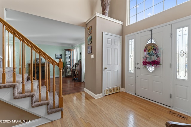 entryway featuring baseboards, visible vents, light wood-style flooring, stairs, and crown molding