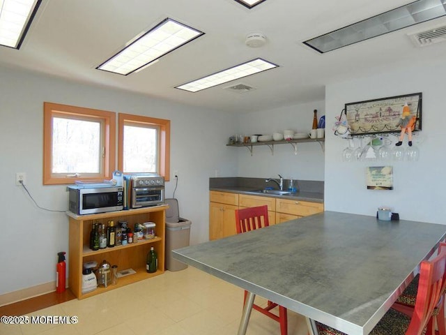 kitchen featuring visible vents, dark countertops, stainless steel microwave, open shelves, and a sink