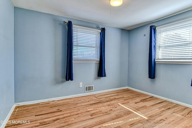 spare room with wood finished floors, visible vents, and baseboards