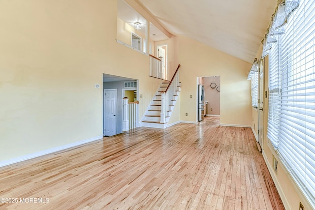 unfurnished living room with light wood-style floors, high vaulted ceiling, baseboards, and stairs