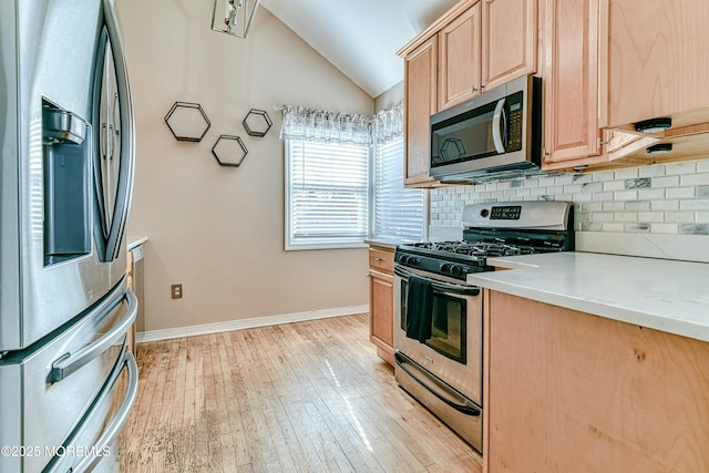 kitchen with tasteful backsplash, lofted ceiling, stainless steel appliances, light countertops, and light brown cabinetry