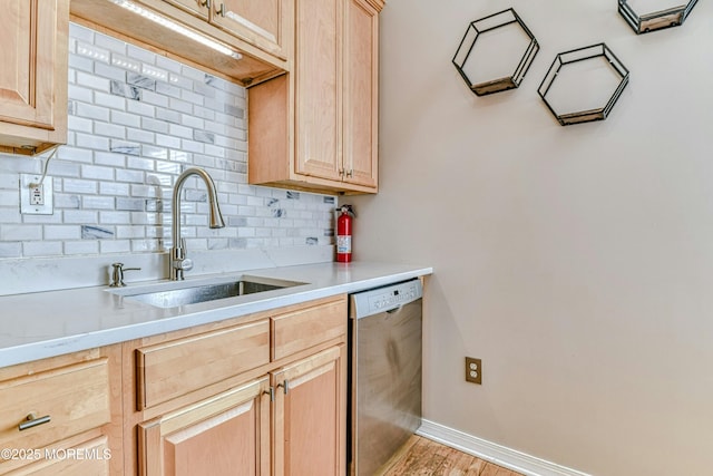 kitchen featuring a sink, baseboards, backsplash, dishwasher, and light brown cabinetry