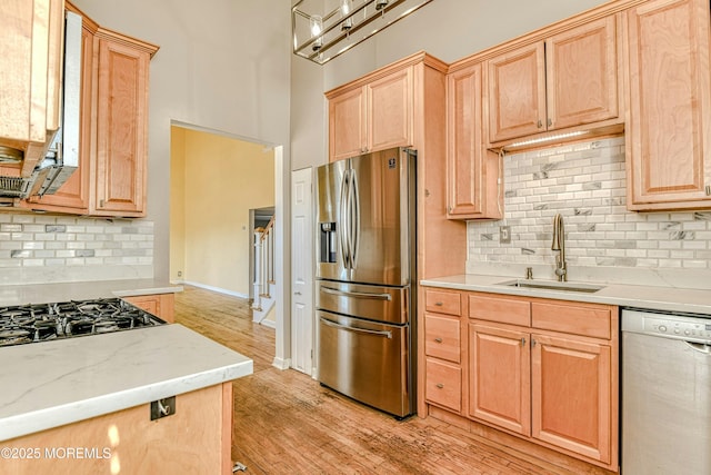 kitchen featuring stainless steel appliances, a sink, light wood-type flooring, backsplash, and light brown cabinetry