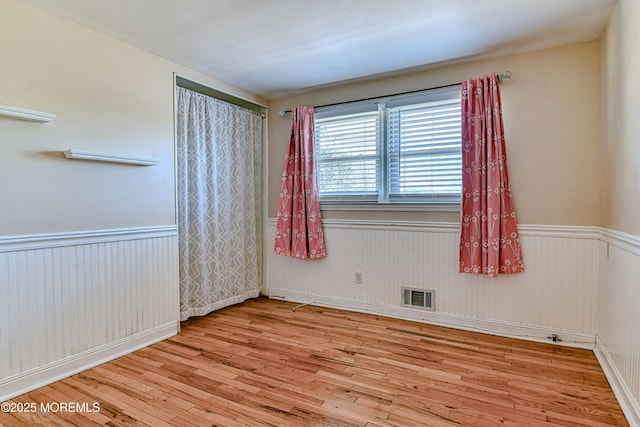 spare room featuring wainscoting, wood finished floors, and visible vents