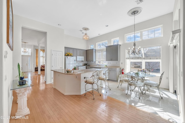 kitchen with a center island, white appliances, gray cabinetry, and an inviting chandelier