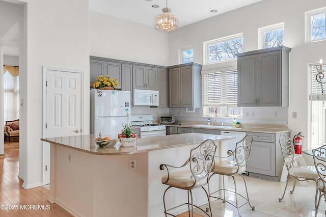 kitchen featuring white appliances, backsplash, a towering ceiling, and gray cabinetry