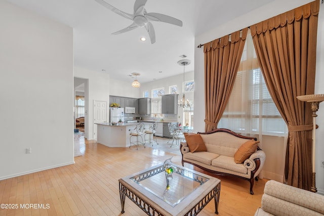 living area with ceiling fan with notable chandelier, baseboards, and light wood-style floors